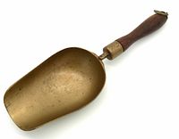 Large antique brass mercantile scoop with a wooden handle and hanging ring at the end.