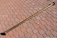Full length view of large brass bar rail placed diagonally on brick-paved ground, showing overall length and condition.