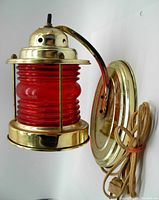 Side view of brass nautical wall sconce with red ribbed glass globe, electric cord, and plug visible.