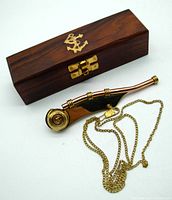 Closed wooden box with brass anchor emblem and brass clasp alongside the brass and copper boatswain whistle with attached chain.