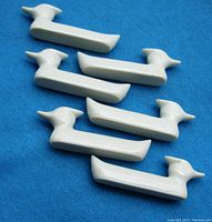 Six white ceramic chopstick rests shaped like stylized ducks, arranged on blue background