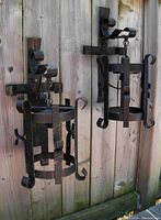 Two black wrought iron wall sconces mounted on wooden fence, showing overall size and style.
