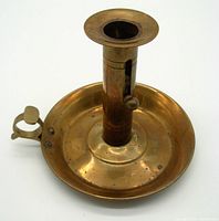 Front angle view of vintage brass chamber stick with finger loop and push-up candle mechanism.