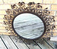 Front view of round mirror with decorative metal leaf frame showing black finish with white splatter and clear reflection.