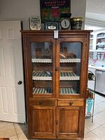 Front view of the antique pie safe cabinet with glass doors showing shelves inside, old tins, and scale on top.