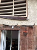 Antique saw displayed above two vintage wooden horse harness yokes hung on a wall with wooden blinds below.