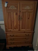 Front view of knotty pine armoire dresser showing two doors with carved panels and four drawers below.