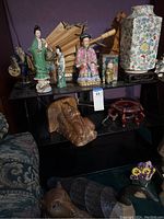 Wide view of shelf with Asian style figurines, umbrellas, large floral vase, and carved duck.