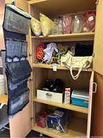 View of inside cabinet showing assortment of decorative glass vases, fabric pillows, assorted bags, plastic containers and black kitchenware items on shelves.