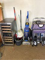 Full view of small wine refrigerator, mop bucket and mop with replacement mop heads, upright carpet cleaner, foldable wagon with star fabric, and metal walker with wheels