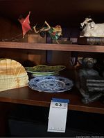 Shelf with monkey figurine holding umbrella, decorative shell, multicolored floral dish, Flow Blue plate, and metal monkey bookends