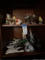 Overall view of two shelves displaying various figurines including multiple cats, birds, and nesting dolls.