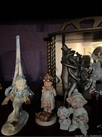 Photo showing mini figurines including a Dopey figure, child figurine with glasses, and two-dance bear figurine in front of a decorative wooden shelf with mirror backing.