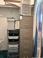 Photo of four drawer beige metal file cabinet by Steelmaster with two travel filing boxes on top and a crafters rolling cart with black and white drawers beside it.