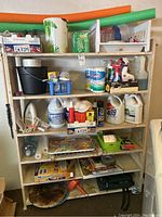 Front view of the garage shelf loaded with a variety of household, cleaning, and laundry items.