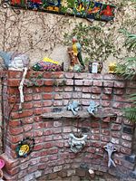 Wide shot of garden brick wall with various ceramic sculptures including frogs, fish, and a tile shelf with multiple decorated tiles arranged on top.