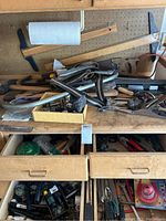 Workbench with assorted hand tools including saws, axes, and small hardware on and under the bench