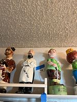 Ceramic liquor figurines and character figurines on shelf, variety of colors and poses.