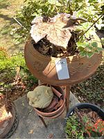 Large terracotta-colored ornate metal plant stand outdoors with decorative metal leaf sculpture on top and several pots underneath.