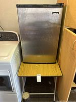 Front view of Magic Chef mini fridge on top of small folding table, showing fridge door and table surface.