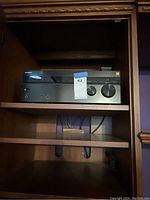 Sony audio receiver inside wooden shelf with visible front panel controls and a label on it