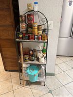 Front view of the metal kitchen shelf with antique tins and compost cans arranged on the shelves.