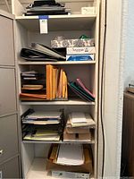 Full view of five-tier white shelf filled with office supplies, paper, folders, and boxes.