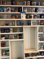 Two photos showing multiple shelves filled with various shot glasses featuring different designs, locations, and colors.