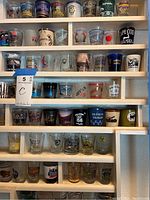 Photo of multiple shelves filled with different shot glasses featuring various designs and logos from multiple locations.