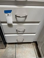 Three white kitchen drawers with metal handles, closed.