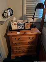 First nightstand with four drawers, Kleenex holders on black tray, and black desk lamp on top.