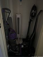 Closely grouped two tower fans and three upright vacuum cleaners in a closet space.