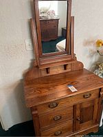 Front view of antique wooden vanity dresser with rectangular attached mirror and closed drawers and door