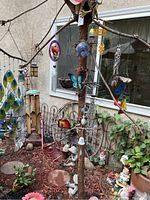 Overview showing multiple wind chimes hanging on a tree branch, along with garden statues such as mushrooms, butterflies, and small yard ornaments in a flower bed setting.
