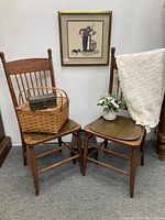Pair of antique wooden chairs with pressed leather seat coverings, carved motif across top backs. Chairs shown with props (basket, box, flowers, cloth) not included.