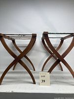 Front side view of two wood folding luggage racks showing curved X-shaped legs and woven straps.