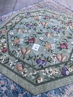 Full view of an octagonal rug laid out on floor, showing green mossy muted background with fruit and flower patterns, central label marked Lot 89.