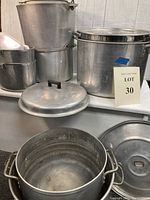 Photo showing 4 very large aluminum pots, 2 medium pots, and 3 lids arranged on a shelf.