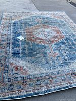Full view of 8x10 rug on pavement showing faded oriental design with blues, grays, orange, and red highlights.