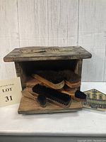 Wooden vintage shoe shine box with five natural bristle brushes on and inside the box. The box has a drop-down door and a ceramic knob, showing rustic worn wood and shabby chic finish.