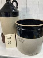 Photo of the one gallon whiskey jug with dark brown to black top and handle, paired with a beige and black two-tone crock.