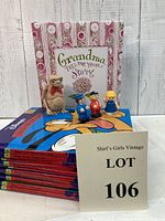 Photo showing 'Grandma Tell Me Your Story' book, 3 plastic child figurines, 1 E.T. figurine, and a stack of Disney children's books with colorful covers
