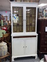 Two-piece white painted mahogany china cabinet with glass upper doors and wooden lower doors. Lightly used with no finish coat on paint.