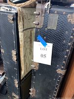 Photo of black antique streamer trunk with patterned exterior showing metal reinforcements and a paper lot number attached.