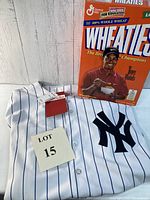 White pinstriped Joe DiMaggio Yankees Mitchell & Ness jersey with tags, next to orange Tiger Woods Wheaties cereal box