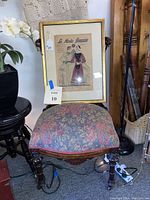Front view of antique Victorian Renaissance chair with floral upholstered seat and framed fashion print resting on the seat.