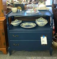 Front view of vintage French style heirloom blue painted maple server with two drawers showing brass handles and open shelf with decorative items on top.