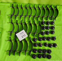 Lot laid out showing 23 dark wrought iron cabinet handles and 27 round cabinet knobs on a green surface, screws included.