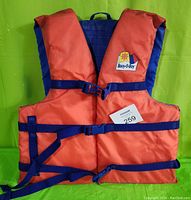 Front view of orange and blue Buoy-O-Boy 780 personal floatation device with three blue straps and logo patch on chest