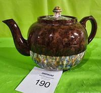 Side view of ceramic teapot showing brown upper half, speckled lower half, and curved spout and handle